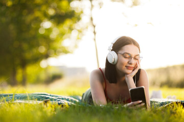 Beautiful dark hair girl listening to music with a headphones from her smartphone. Lying on a green meadow.