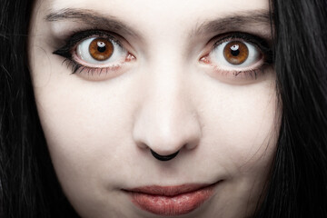 Close up portrait of a goth style girl looking at camera against gray background.