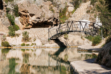 Puente de hierro de forja en piscina natural del municipio de Bolbaite con reflejos en el agua,...