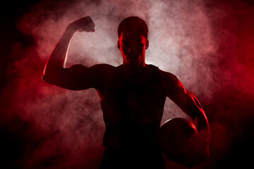 Silhouette basketball player side lit with red color holding a ball with smoke in the background....