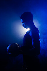Basketball player holding a ball against blue fog background. Muscular african american man silhouette.