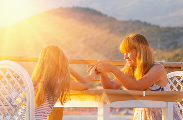 Portrait of happy smiling young mother and beautiful daughter having fun on the sea beach. They hold each other's hands and meet the sunrise. - 784486569