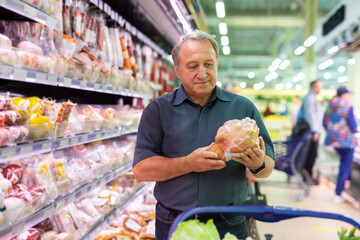 Elderly man chooses chicken meat in supermarket - 784486708