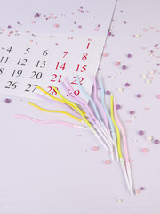 A calendar sheet with dates and candles for the cake are on the table among the sprinkles, a place for text