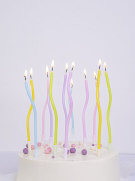 Multicolored pastel lighted candles in a white cake , a place for text
