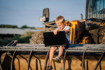 Valmiera, Latvia - August 17, 2024 - A young boy sits on farm machinery, focused on a laptop he is holding.