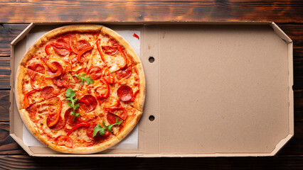 Pepperoni pizza with bell peppers and arugula in open carton box on dark wooden table flat lay with...