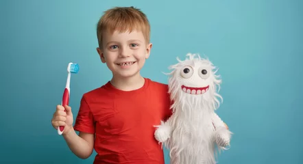 Poster Cute smiling boy holding toothbrush and cute white knitted tooth pattern with eyes isolated on blue background, concept of children's dental health care © Kien