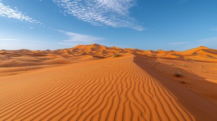   A vast expanse of sand dunes beneath a blue sky with wisps of clouds - obrazy, fototapety, plakaty
