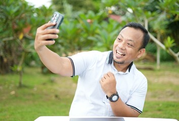 Asian man's expression while holding a cellphone. Asian man is online with mobile phone