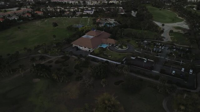 Aerial view of golf club grounds at twilight. Golf course, central structure alongside parking area, surrounded by trees and pathways. Cocotal golf, Dominican, Punta Cana