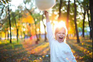 Little cute girl with cotton candy in the autumn park background. Having fun and posing