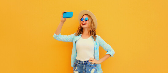 Happy smiling young woman taking selfie with smartphone wearing straw hat on yellow background