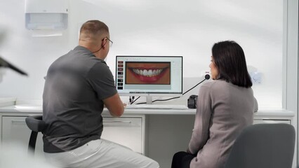 Cosmetic dentist showing photo of teeth smile to female patient on screen in modern dental clinic. Stomatologist and patient discuss modeling of veneers. Doctor explains photo of teeth to a woman.