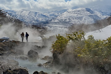 Iturup. Russia.  March 18, 2023. Tourists admire the steam of the picturesque thermal spring (Boiling River) near the Baranovsky volcano, the water temperature in the source of which is 80 degrees.