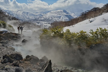 Iturup. Russia.  March 18, 2023. Tourists admire the steam of the picturesque thermal spring...