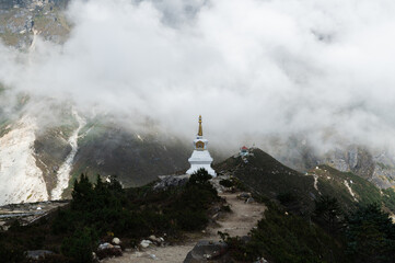 View of Buddhist Stupa and low clouds and mountains in Thame village during trekking in Nepal....