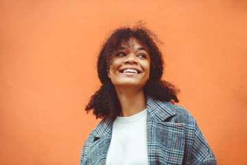Happy African ethnicity girl with dark curly hairstyle in stylish coat looking aside and smiling