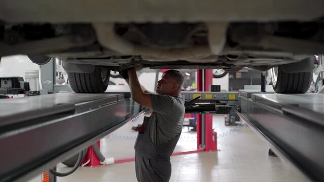Auto mechanic performs wheel alignment in garage. Expert calibrates car tires using specialized equip, ensures precise driving. Professional service tech adjusts axles in modern workshop.