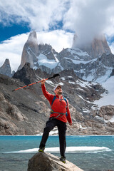 Naklejka premium Caminante alzando su bastón en señal de triunfo por subir hasta la Laguna de Los Tres, en el Chalten, Patagonia. El pico del cerro Fitz Roy de fondo