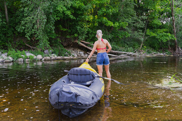 A girl with a rubber boat on the river on a summer day.