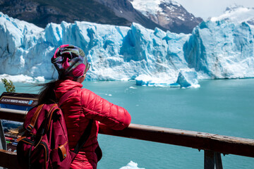 Turista mujer con campera roja mirando el Glaciar Perito Moreno, desde las pasarelas del Parque Nacional Los Glaciares	 - obrazy, fototapety, plakaty