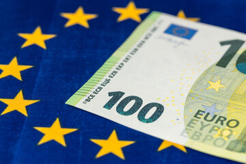 100 euro banknote against the background of the flag of the European Union, EU financial concept, Joining the euro zone, Common monetary policy.