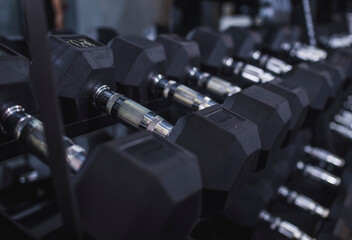 Naklejka premium Close-up view of a row of black hex dumbbells neatly arranged on a rack in a gym, emphasizing fitness and exercise concepts.