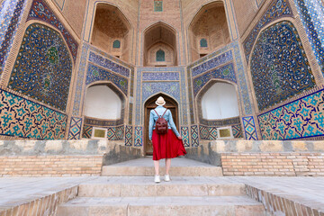Back view of Young woman at Bukhara, Uzbekistan Mir-i-Arab Madrasa Kalyan minaret and tower. Translation on mosque: "Poi Kalyan Mosque"