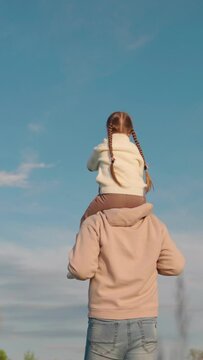 Father child walk together in park. Child sits on his fathers shoulders. Child dream to fly, family travel. Dad plays with his little daughter on his shoulders against sky, fatherhood. Happy family.