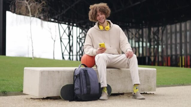 Modern male zoomer using cellphone and looking to the camera. Basketball player and skateboarder.
