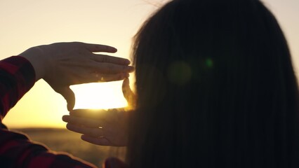 Hands of young female director cameraman making frame gesture at sunset in park. Seeing world as...