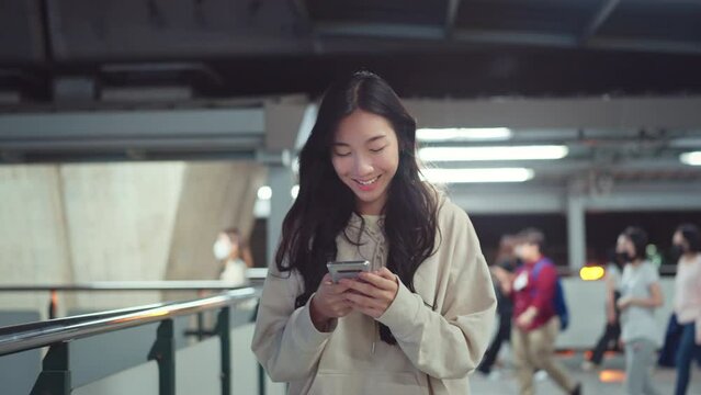 Happy asian woman with smile walking and using smartphone on the street in urban city, Smiling female checking message on mobile phone in town at night.