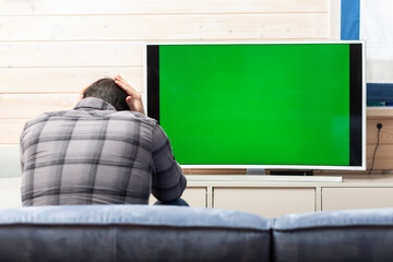 Shocked man on the couch watching tv. Bad news and Green screen concept