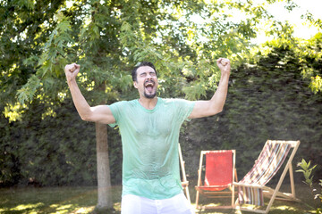 Happy man stands under a stream of splashing water in the hot summer
