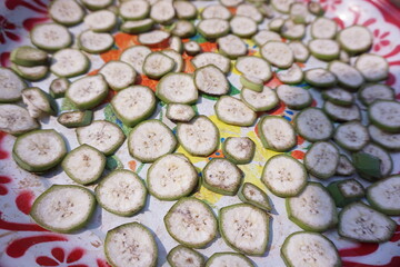 Close-up of raw banana thin slices, a round baked, dried or sun-dried crisp pieces isolated on red tray in the countryside. Herbal concept for health.
