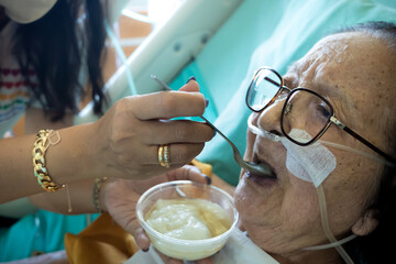 A daughter feeding delicate food to her sick elderly mother in a hospital bed