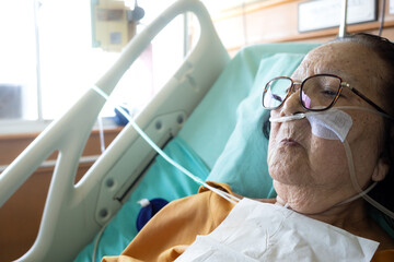 Sick Asian elderly woman lying in hospital bed undergoing inpatient  treatment wearing oxygen tube