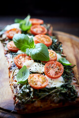 Open-faced toasted cheese sandwich with cherry tomatoes, spinach and fresh basil. Brown wooden background.	