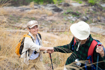 active asian senior couple hiking together on summer time,senior man help his wife trying to climb on the hill,family relationship,elderly pensioner lifestyle,love emotion,travel,adventure