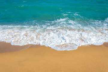 Fototapeta na wymiar A frothy blue ocean wave on a clean sandy sea beach.