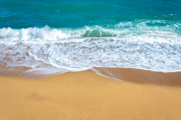 Blue ocean wave, sea foam, clean sandy beach.