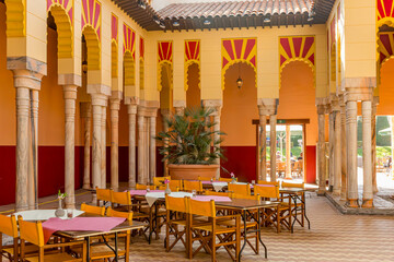 Fototapeta na wymiar Replica of pillars and walls of Cordoba mosque in open interior patio of restaurant, Dutch theme park, wooden tables and chairs, sunny day in South Limburg, Netherlands