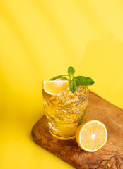 A glass of iced tea with lemon and mint on a wooden board on a yellow  background with a shadow.