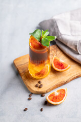Coffee with orange juice (bumble) in a tall glass with ice and mint on a wooden board on a light background