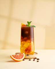 Americano coffee with orange juice (bumble) in a tall glass with ice and mint on a yellow background with coffee beans, shadows and citrus fruits. Trendy summer Asian refreshing drink. - obrazy, fototapety, plakaty