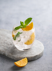 Lemonade tonic drink with fresh lemon, mint and ice on a marble board on a light background.