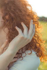 A woman's hand touches red curly hair. Redhead curly hair close-up