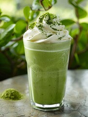 A refreshing matcha green tea frappuccino, crowned with a perfect peak of whipped cream and a sprinkle of green tea powder The beverage is placed on a natural stone countertop, with a background of lu