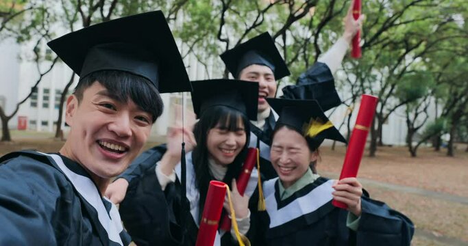 Four Asian graduates joyfully wave their diploma tubes, celebrating the completion of their studies.